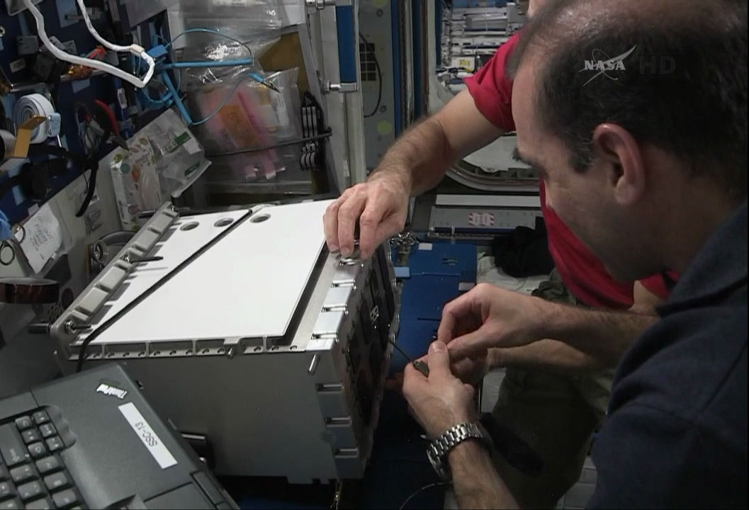 Rick Mastracchio et Steve Swanson en train d'installer un nouveau circuit intérieur d'un multiplexeur-démultiplexeur MDM de rechange à bord de l'ISS en prévision de l'EVA 26 (source NASA TV)