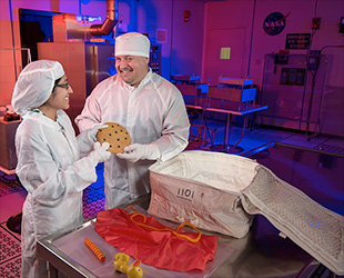 Des techniciens emballent le cookie de Cookie Monster et autres objets de Sesame Street pour voler dans l'espace à bord de l'Orion EFT-1. (NASA)