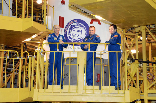 Les astro/cosmonautes Jeff Williams, Alexey Ovchinin et Oleg Skripochka posant devant la coiffe du lanceur Soyuz TMA-20M arborant le logo de l'année Gagarine (Credit: RSC Energia)